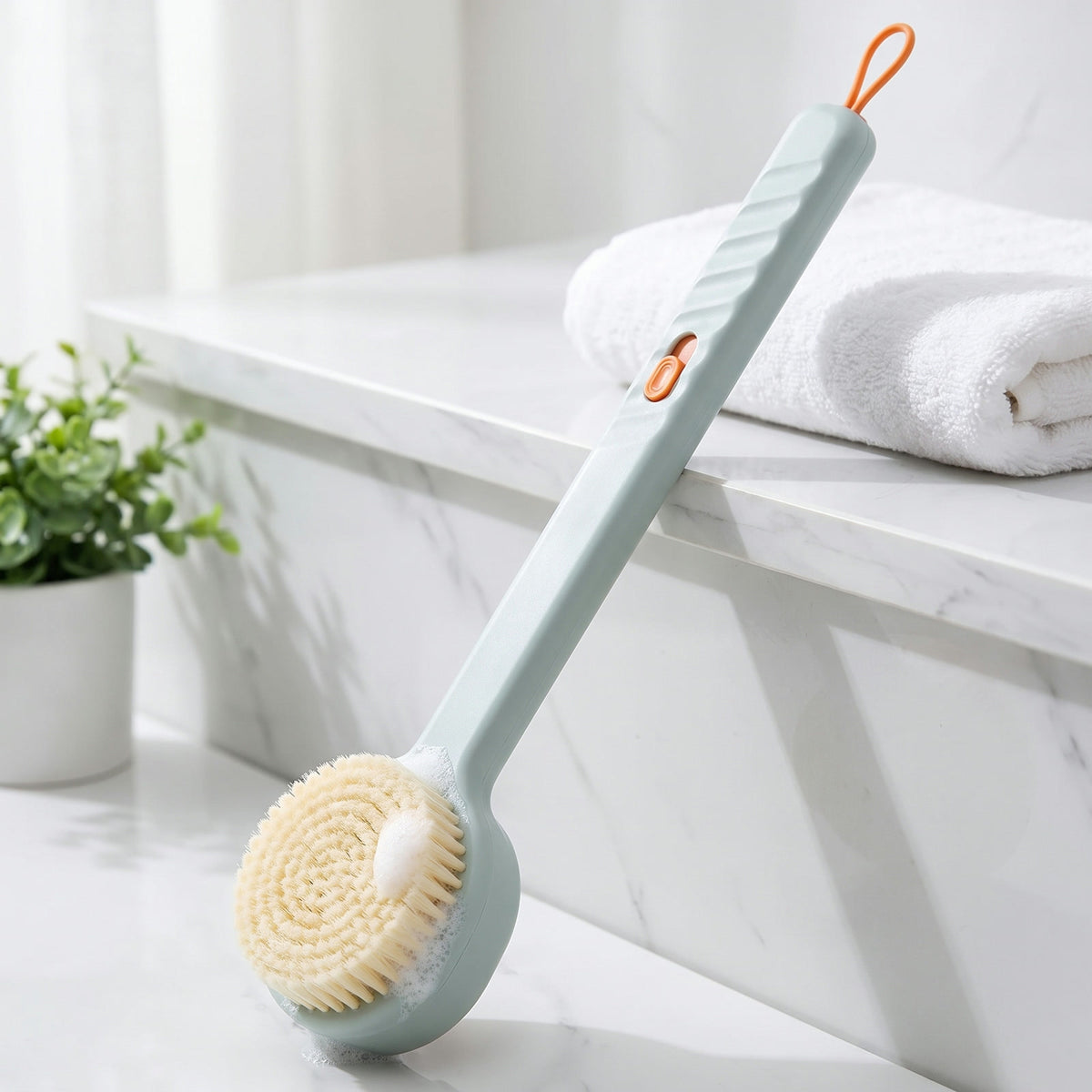 Lather Reach Back Brush in Sage Blue: soap-dispensing long handle shower brush with soft bristles on a bathroom shelf