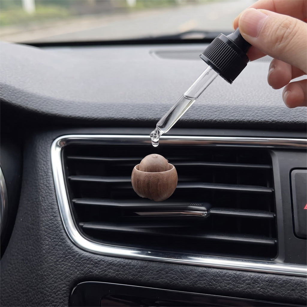 A glass dropper puts two drops of essential oil onto the wood ball of a car vent diffuser