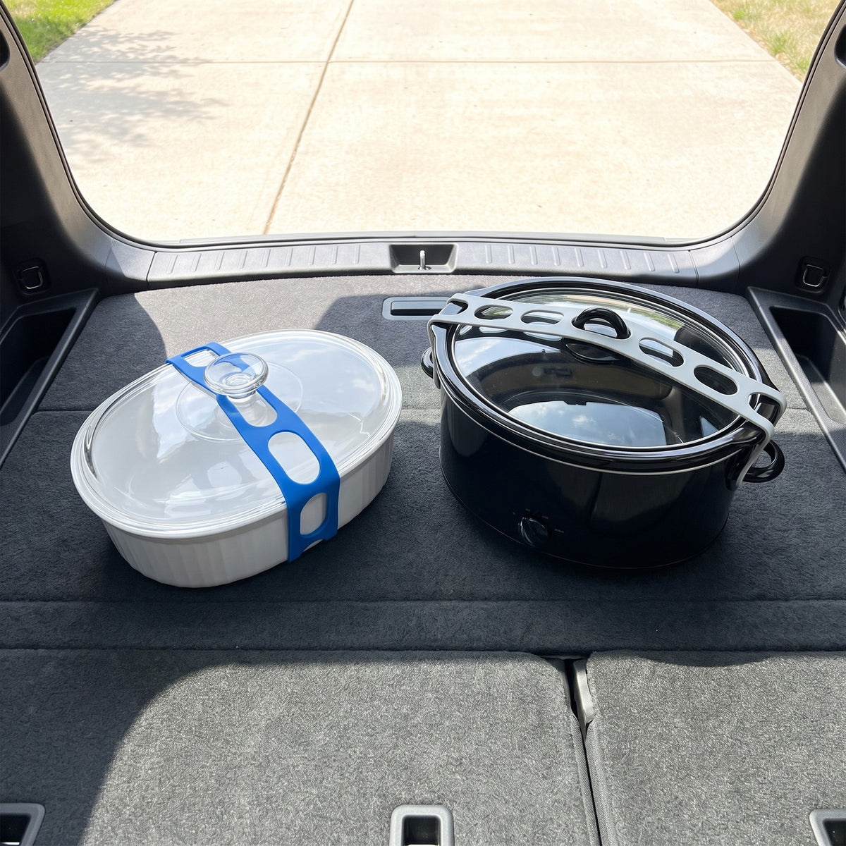 Casserole dish and slow cooker in a car trunk, each lid held down by a lid strap