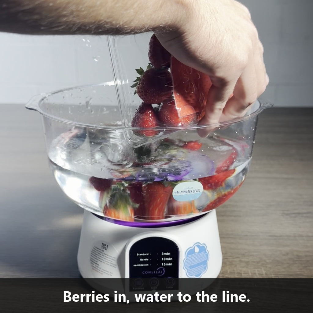 Pouring a box of strawberries into the Vortex Produce Washer bowl of water