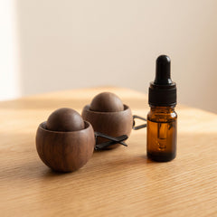 Wooden Car Vent Diffuser: a solid wood ball fixed in its wood cup with a black vent clip, next to an amber bottle of essential oil